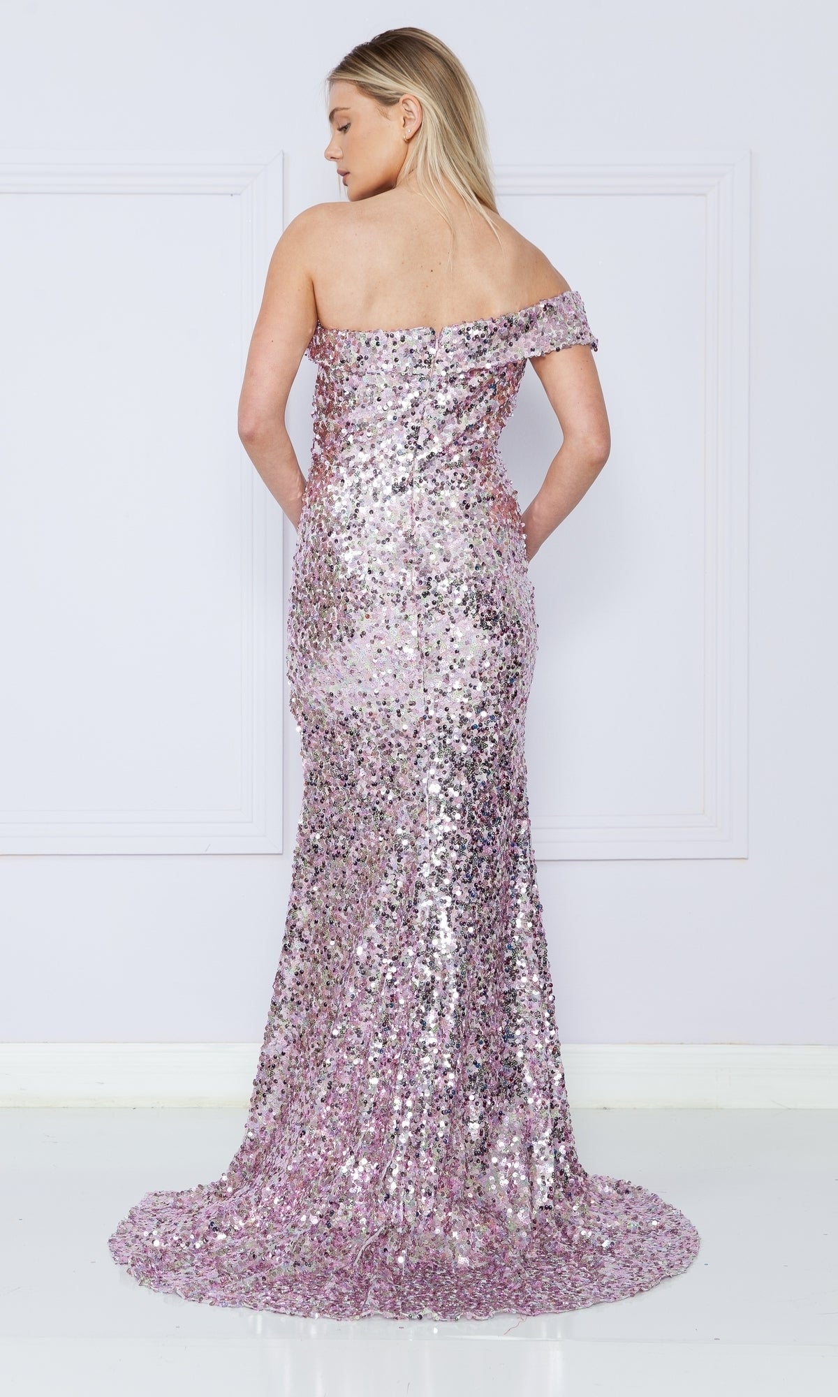 A woman stands facing away in the One-Shoulder Long Sequin Prom Dress 9180—a pink formal gown with shimmering sequins and a slight train flowing to the floor.